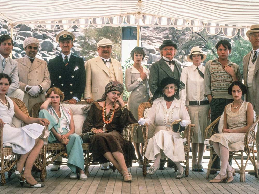 A group of people, half seated and half stood up, all posing for a group photo. All dressed in 1930s clothes and under a gazebo.