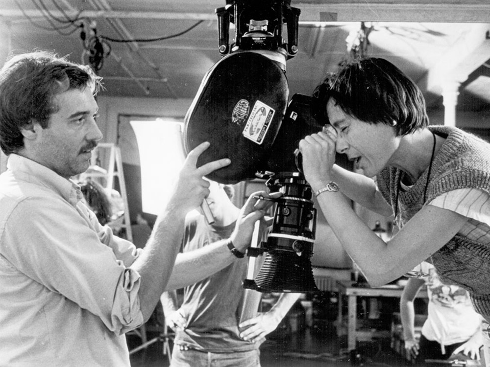 Yvonne Rainer looks down a camera towards a man preparing the camera