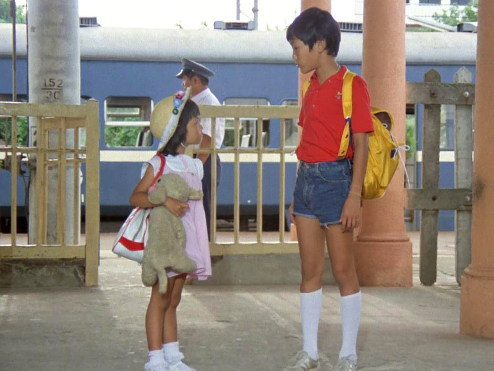 Two young Taiwanese children stand at a train station, staring at one another