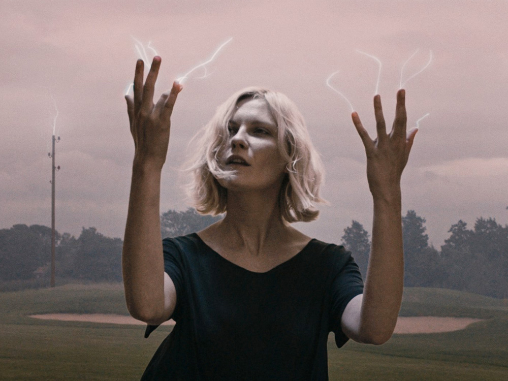 [alt](A blonde white woman holds her hands up against a foggy golf course. Wisps of light emerge from her fingertips)