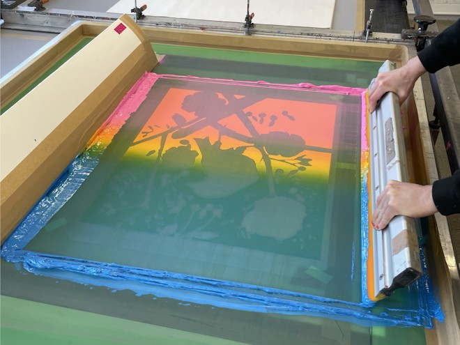 A pair of hands screen printing the Ann Craven print, in colourful red, yellow blue-green