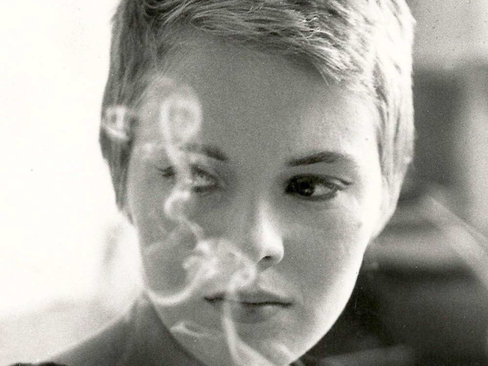 A sepia image of a woman with short blonde hair, smoke trailing in front of her face