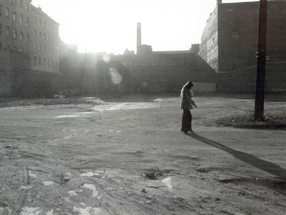 A person walks through a black and white field surrounded by industrial buildings in Berlin