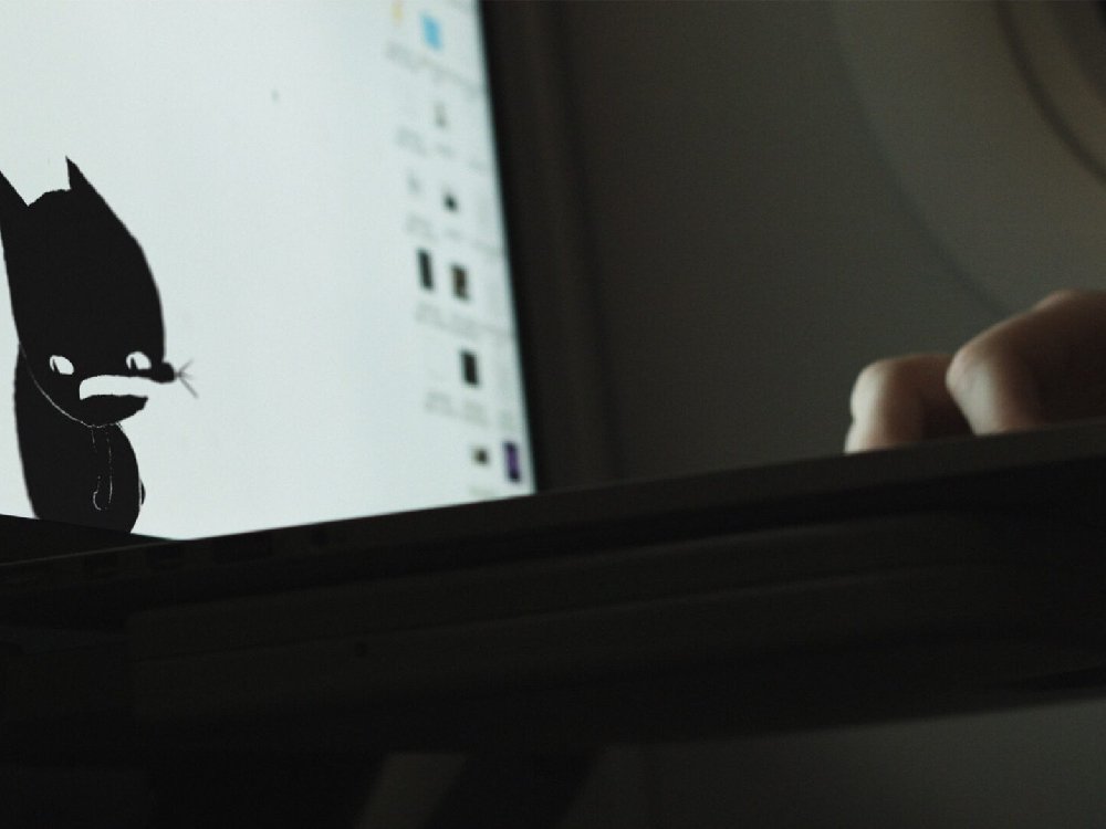 close up of a laptop, an animated black cat is on the screen against a white desktop background