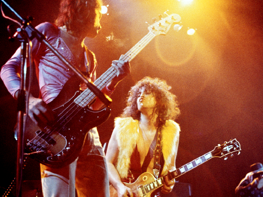 Two glam rock musicians play electric guitar on stage