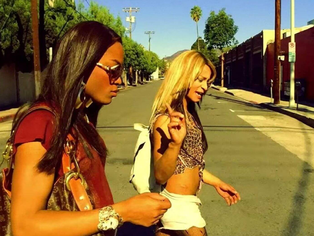 Two women cross the street in LA, blue sky and palm trees in the back