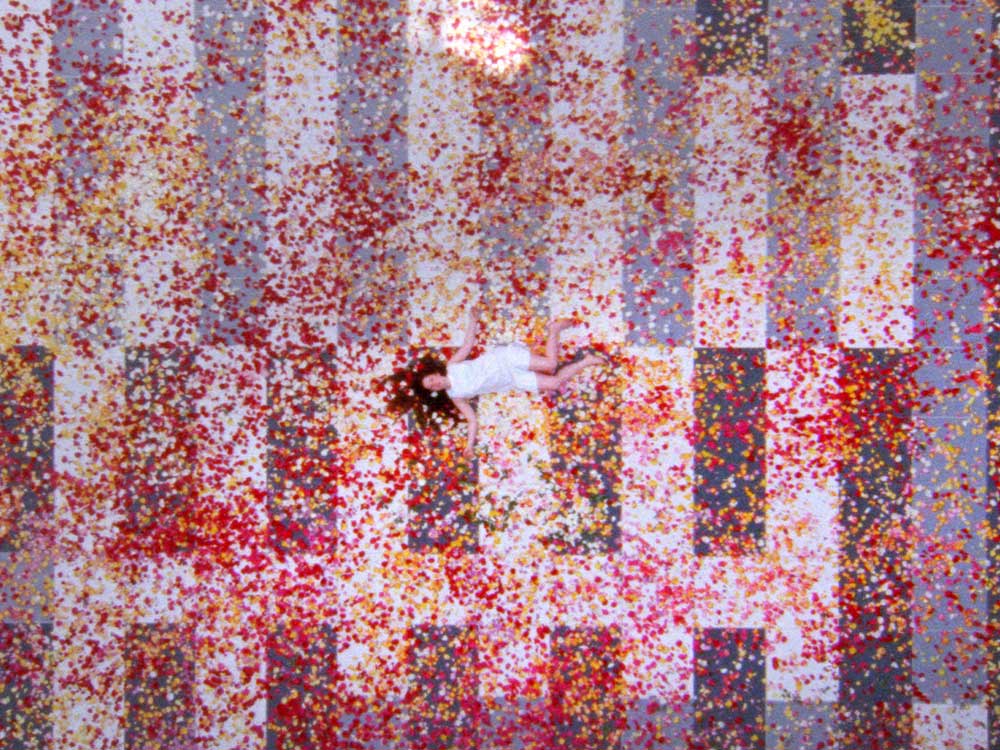 A person in white lies down on a floor of red and yellow petals