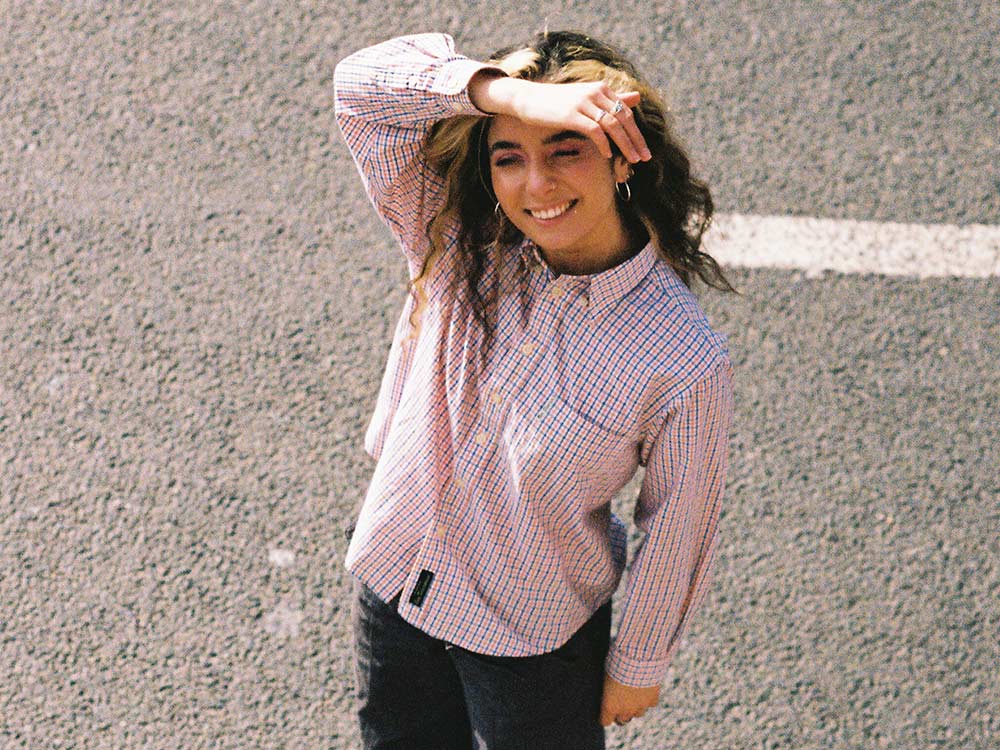 An image of Jasmine Jethwa, smiling and squinting in the sun on an asphalt road