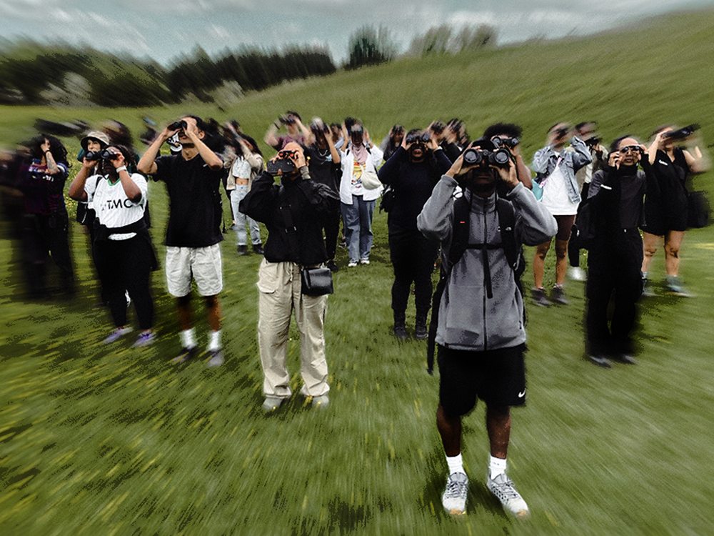 A group of hikers hold binoculars up, looking at the sky