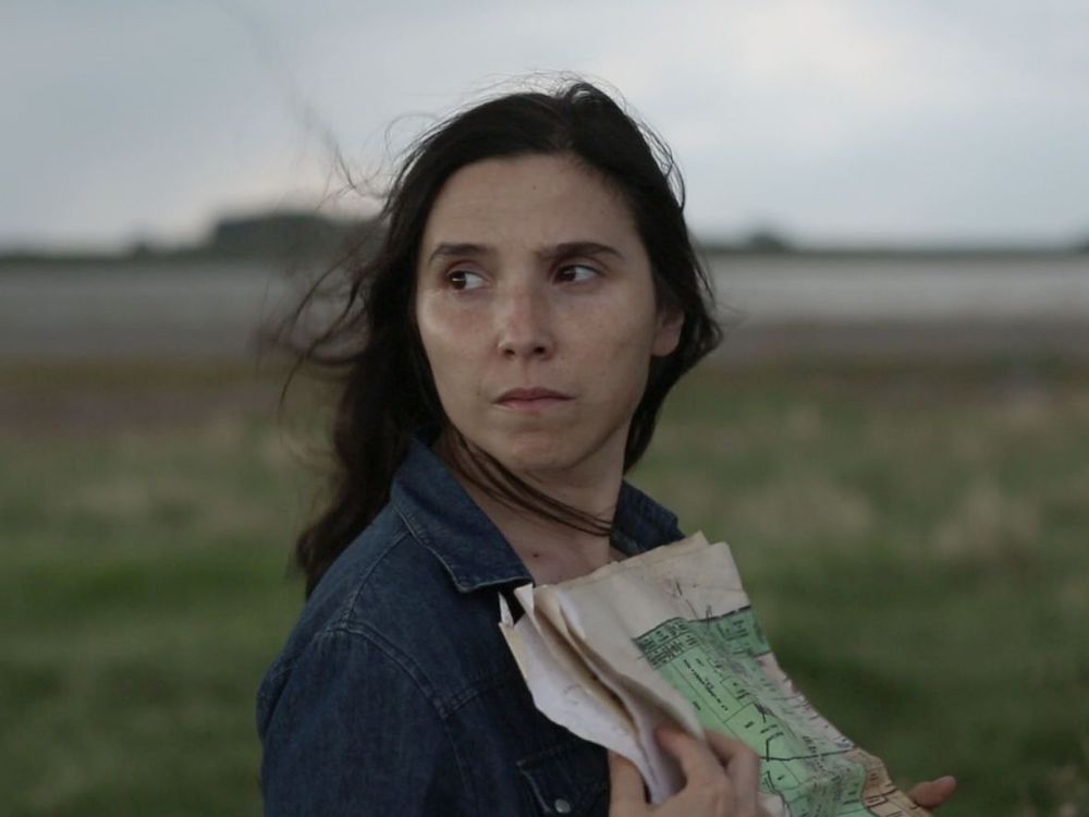 A woman stands in a dark, grassy field with a map