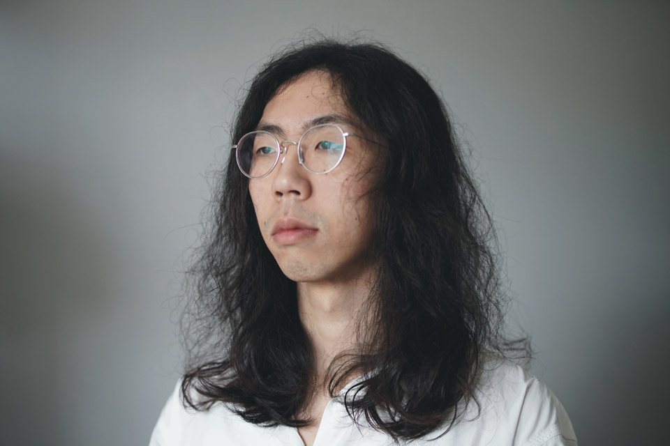 The artist Gary Zhexi Zhang, an East Asian person with long shoulder-length hair and round framed glasses