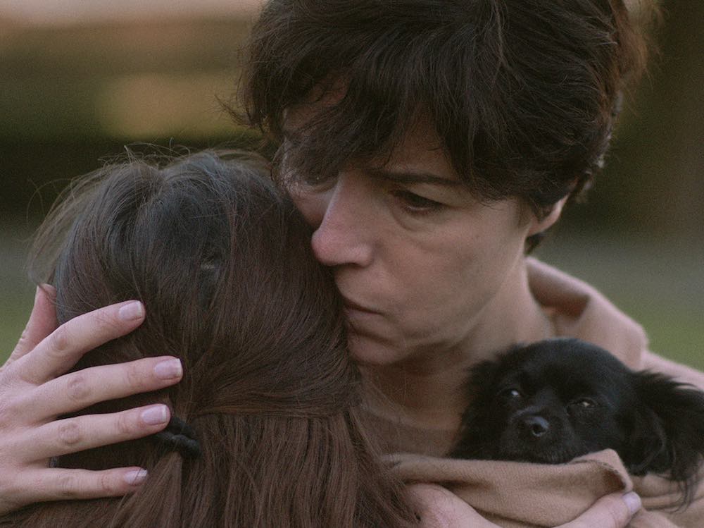 A mother holds her daughter. A small black dog is tucked in her scarf