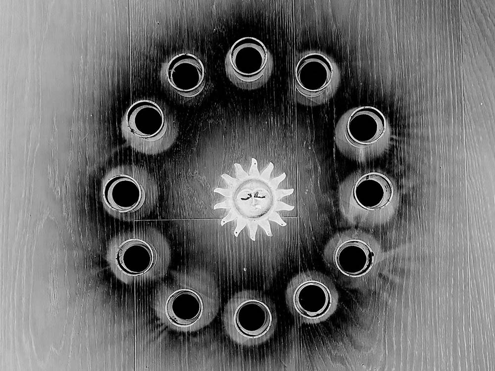 A ring of black shadowy circles surrounding a sun, etched or burned onto wood