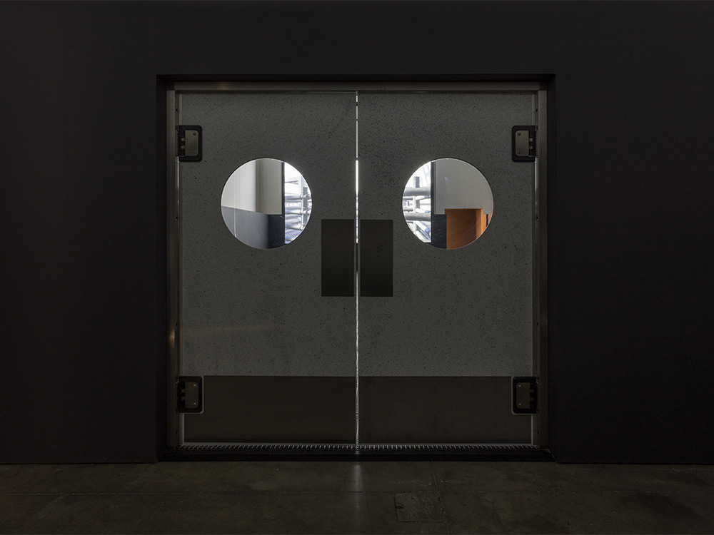 Metal abattoir doors closed in front of a darkened screening room showing a single hanging screen